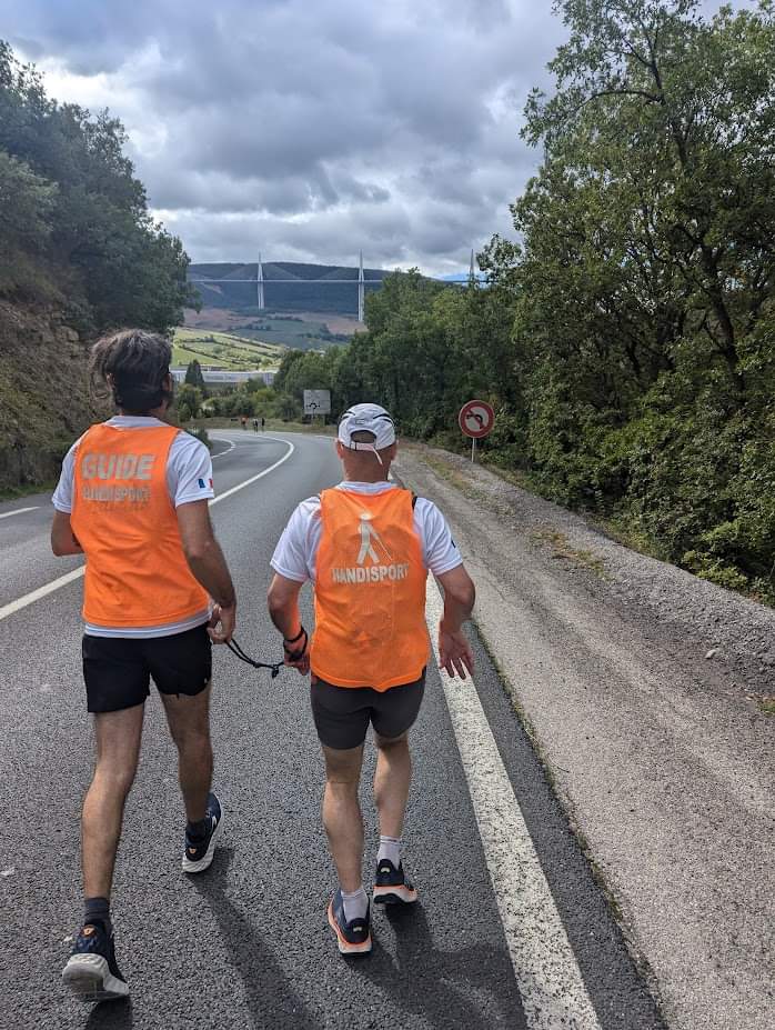 Nicolas et son guide Erwan de dos sur les 100 km, face à eux : le viaduc de Millau